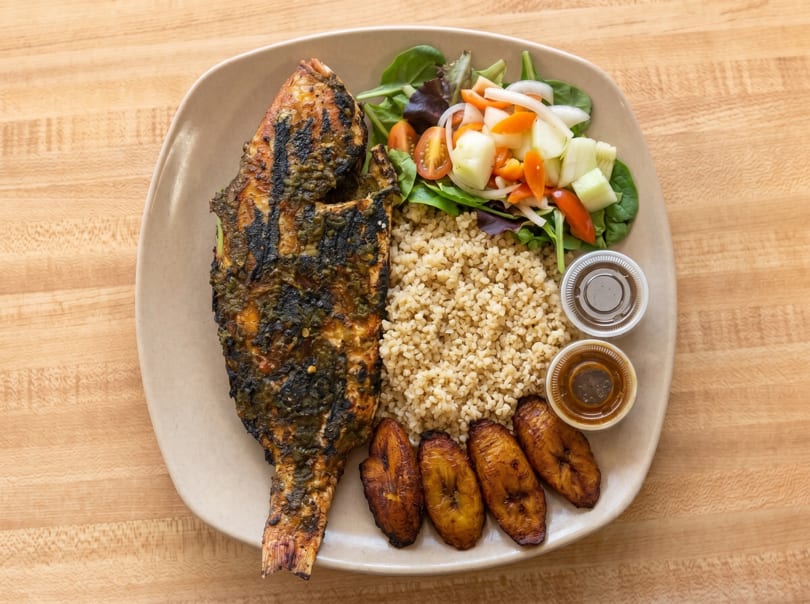 Grilled whole fish with rice, fried plantains, a fresh salad, and two dipping sauces.