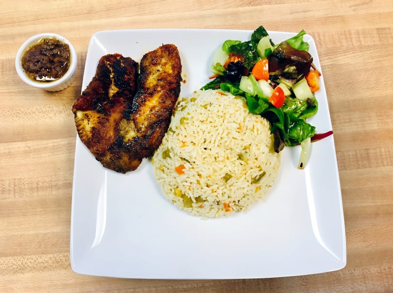 Grilled fish with rice, a side salad, and a small dish of sauce on a white plate.