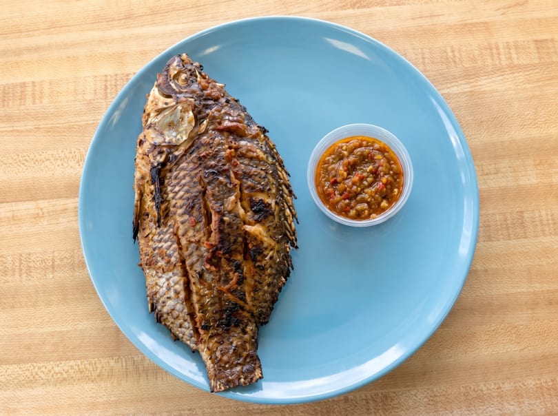 Grilled whole fish with crispy skin and a side of spicy sauce on a blue plate.