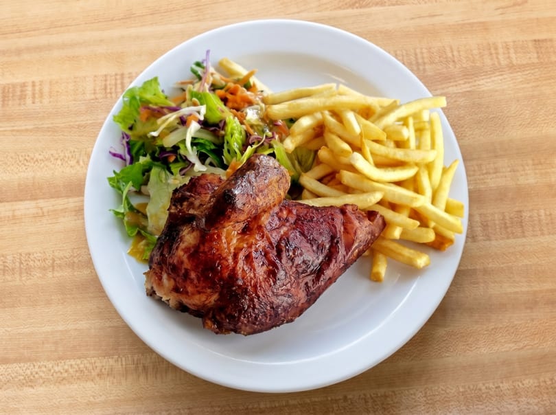 A plate of roasted chicken, golden fries, and a fresh green salad on a wooden table.