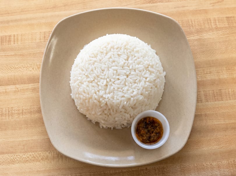 A mound of white rice and a small cup of brown sauce on a beige plate.